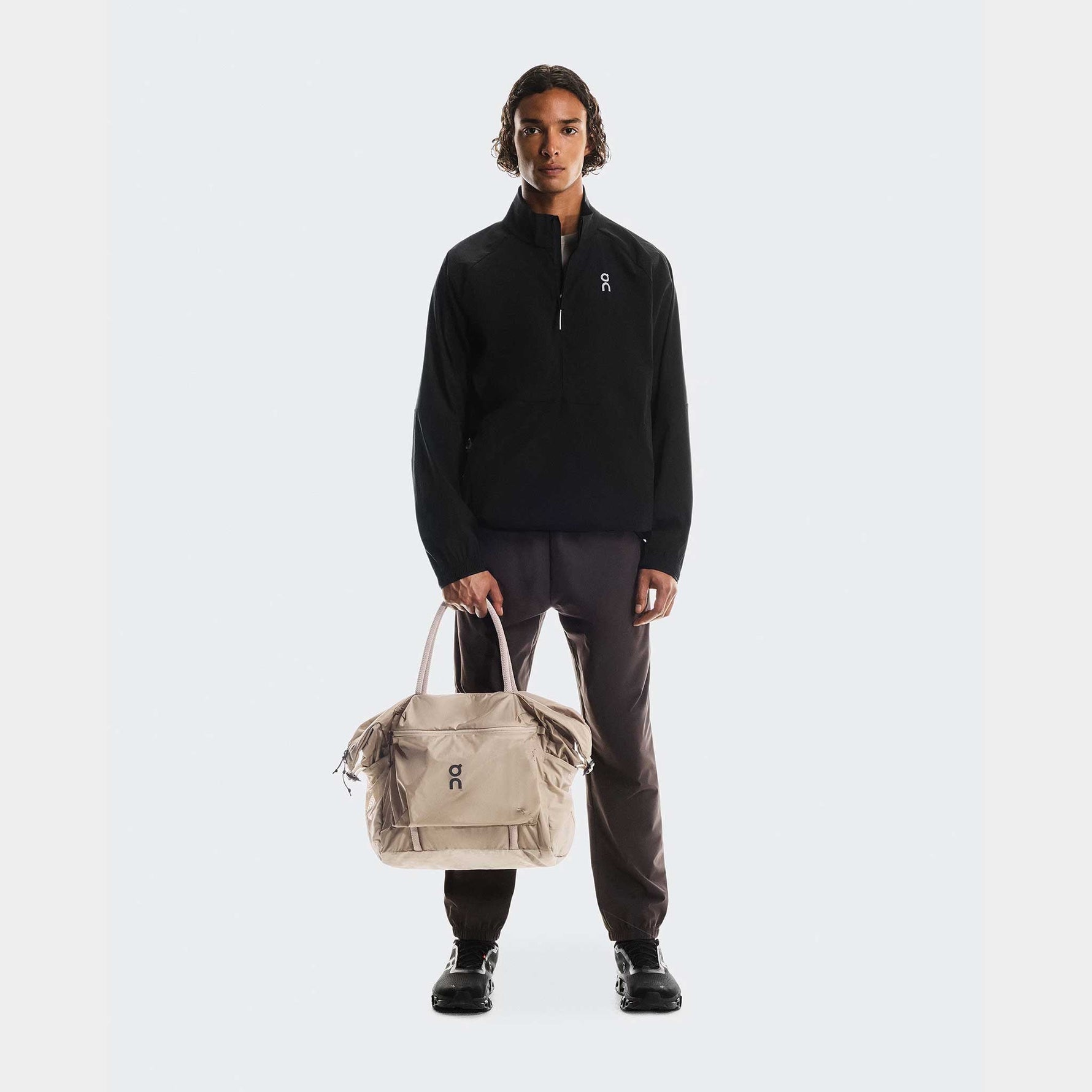 Model holding On Track Pack 35L Lite in sand color against white background