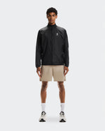 Man wearing On 5 inch Core Shorts in desert beige color with black jacket