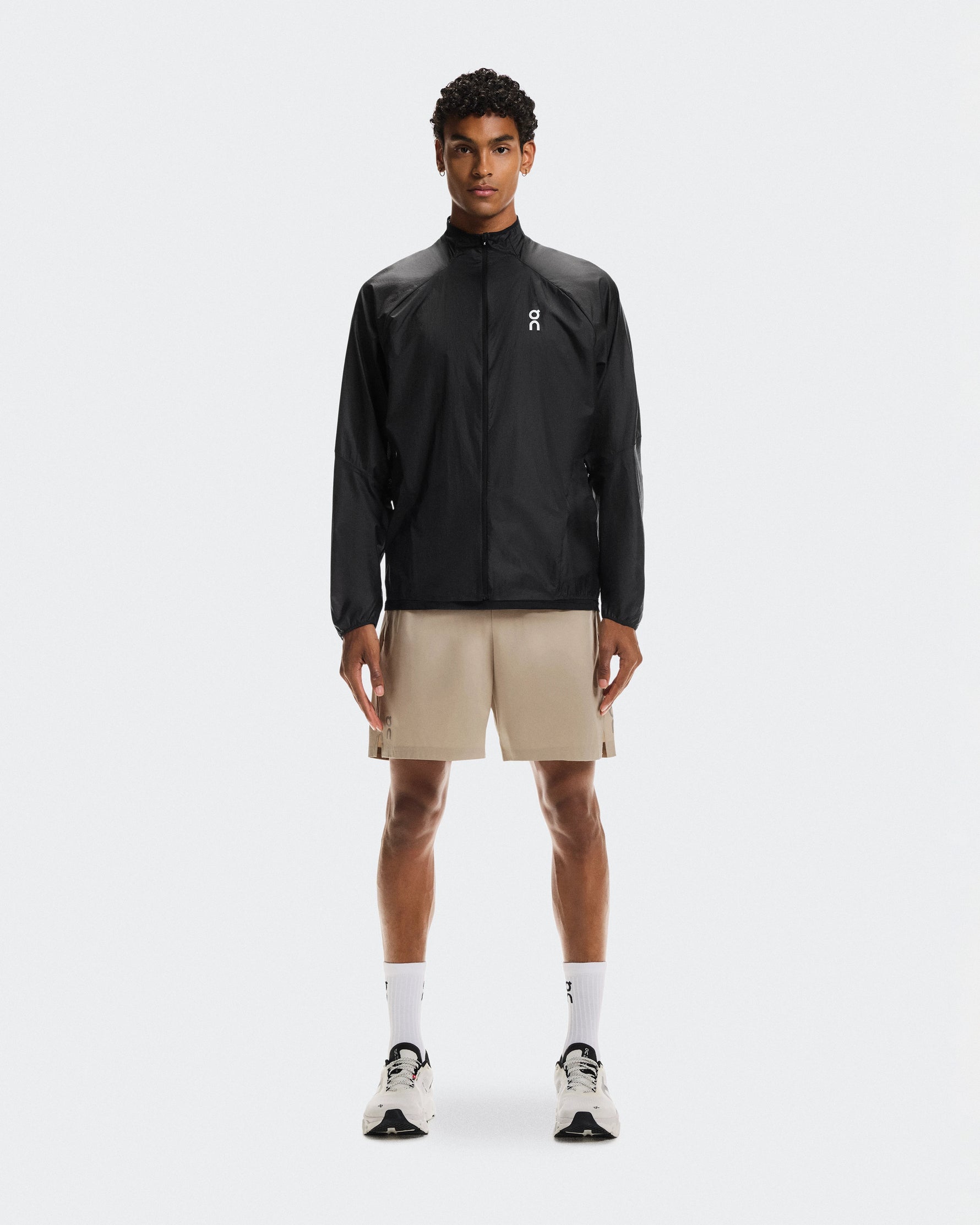 Man wearing On 5 inch Core Shorts in desert beige color with black jacket