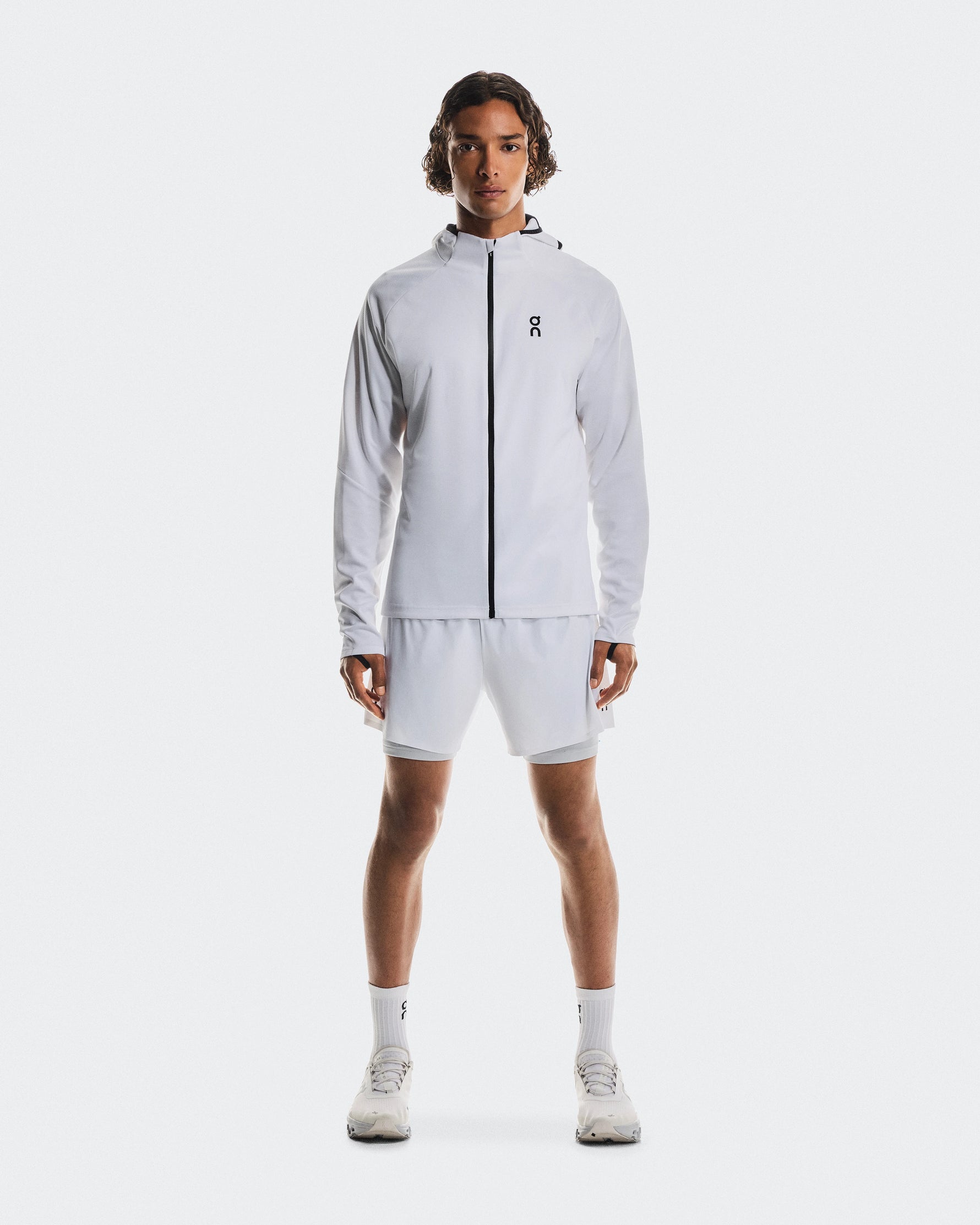 Male model wearing On white hooded jacket and white performance shorts with sneakers