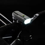 Lezyne Macro Drive 1400+ front light illuminated on bike handlebar, held by gloved hand in dark setting