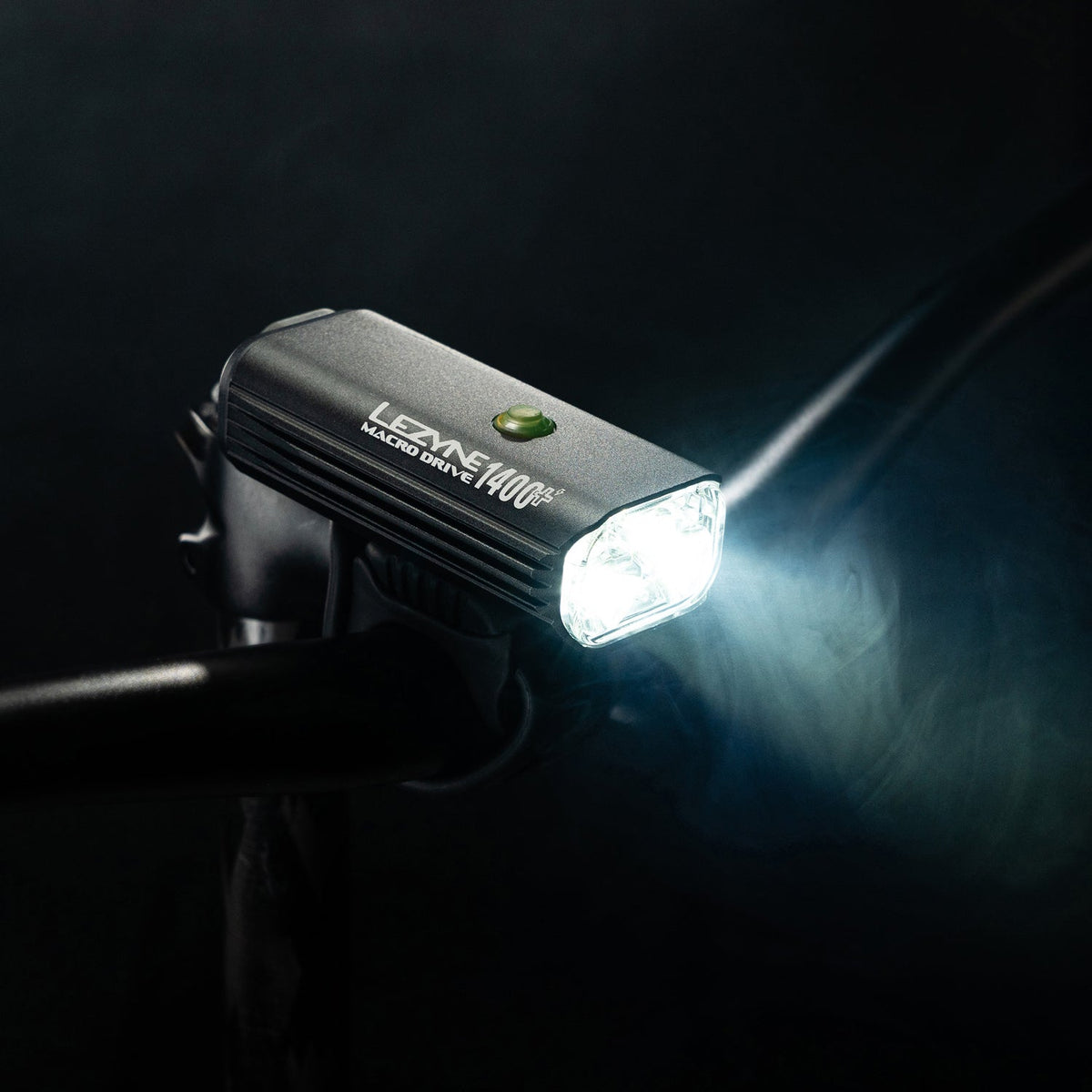 Lezyne Macro Drive 1400+ front light shining brightly on handlebar mount against dark background