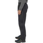 Man wearing black Patagonia Torrentshell 3L pants with hiking shoes on white background