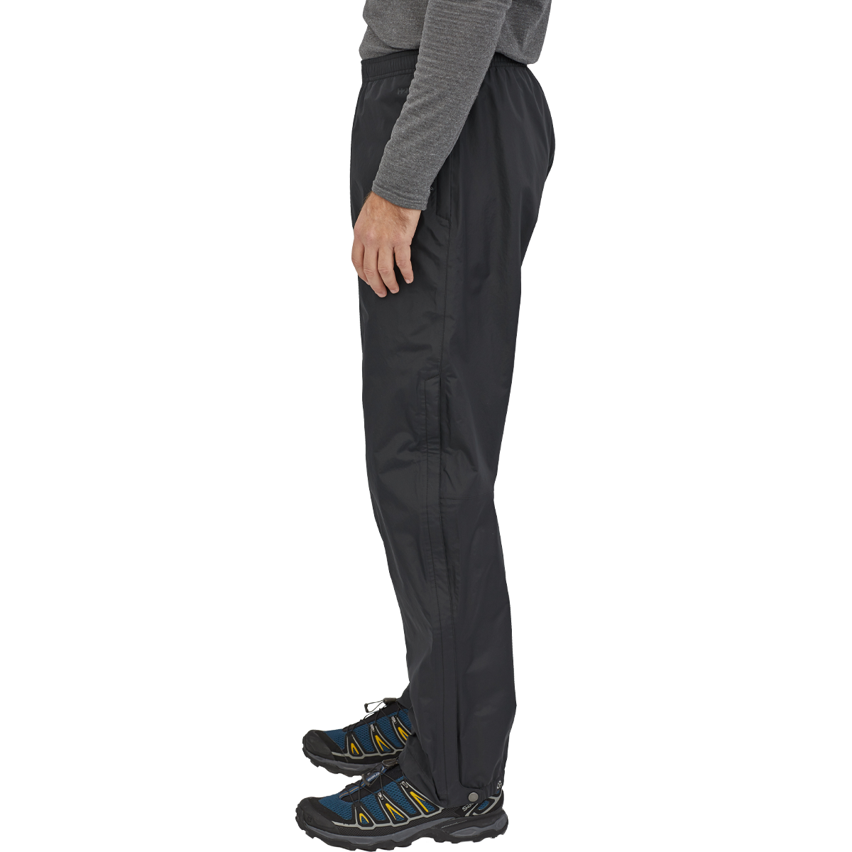 Man wearing black Patagonia Torrentshell 3L pants with hiking shoes on white background