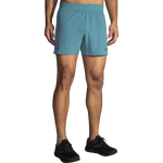 Male model wearing Brooks Sherpa 5-inch running shorts in Storm Blue, front view with black Brooks running shoes