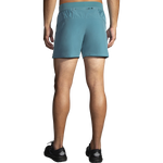 Rear view of male model wearing Brooks Sherpa 5-inch men's running shorts in Storm Blue with black Brooks shoes