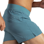 Close-up side view of Brooks Sherpa 5-inch men's shorts in Storm Blue showing perforated mesh side pocket detail on male model