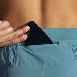 Detail shot of Brooks Sherpa 5-inch men's shorts Storm Blue showing smartphone being inserted into zippered back pocket