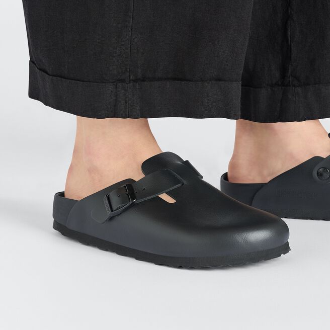 Black Birkenstock Boston clogs worn with dark pants against white background