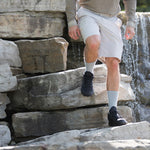 Man wearing Thorlos grey hiking crew socks with black shoes climbing rocky steps near waterfall