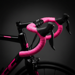 Pink geometric patterned bar tape wrapped on black bicycle handlebars against dark background