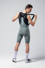 Man wearing Gobik Matt 2.0 bib shorts in sage green putting on suspenders