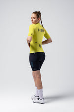 Female cyclist wearing bright yellow Gobik CX jersey and black shorts in studio setting