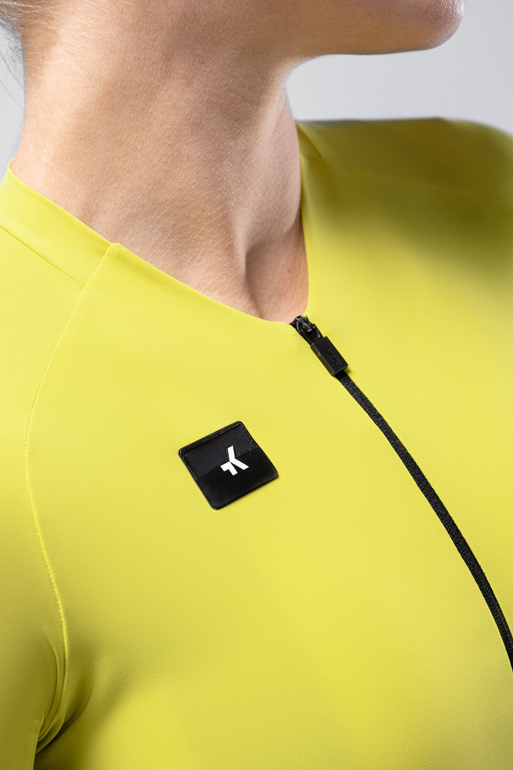 Close-up of yellow Gobik cycling jersey with black logo patch and zipper detail