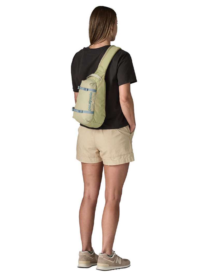 Woman wearing Patagonia Atom Sling 8L in olive green, shown from behind