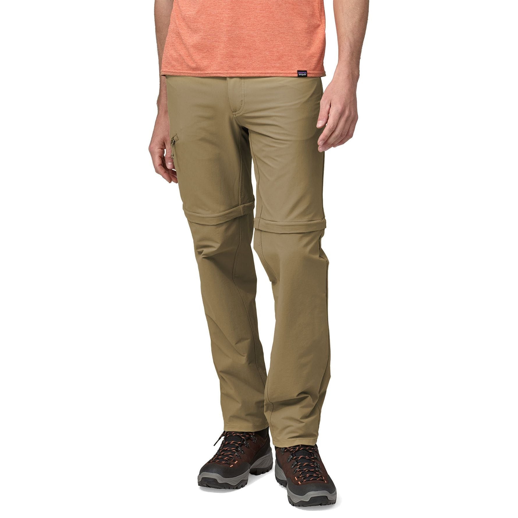 Man wearing Patagonia tan convertible hiking pants with orange shirt and brown boots