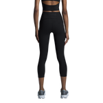 Woman wearing black On Studio 7/8 tights with matching sports bra on white background