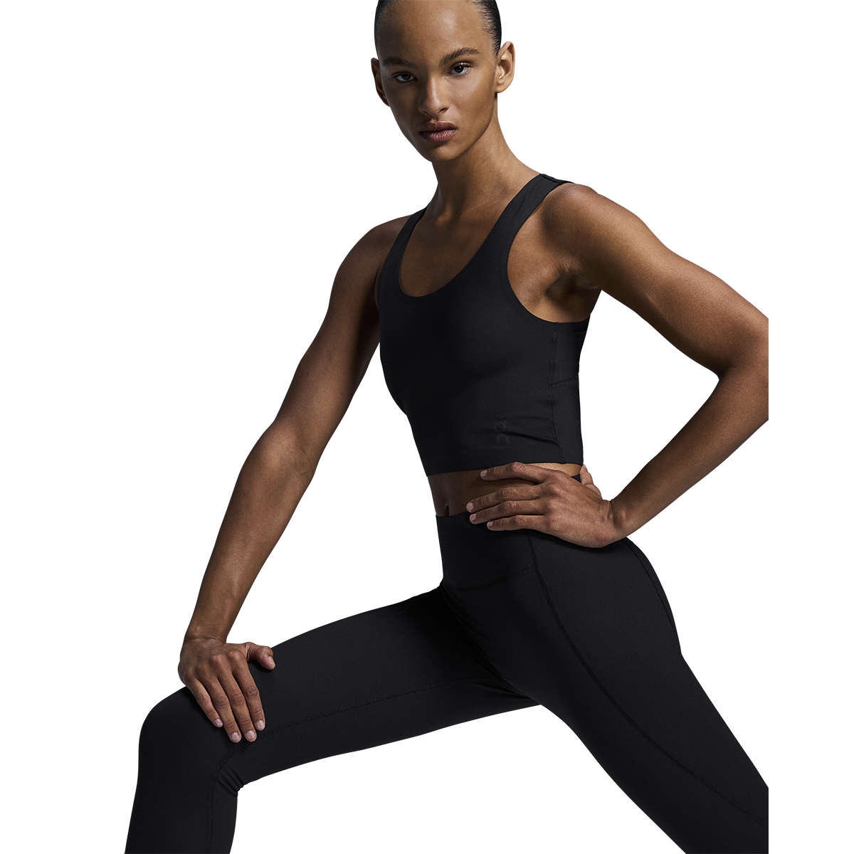 Woman wearing black On Studio Tights and sports bra in athletic pose