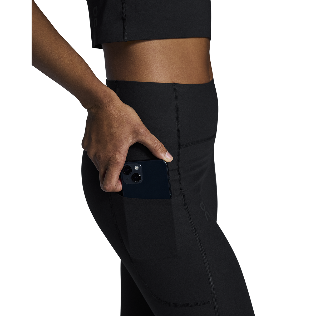 Woman wearing black On Studio Tights with side pocket holding smartphone