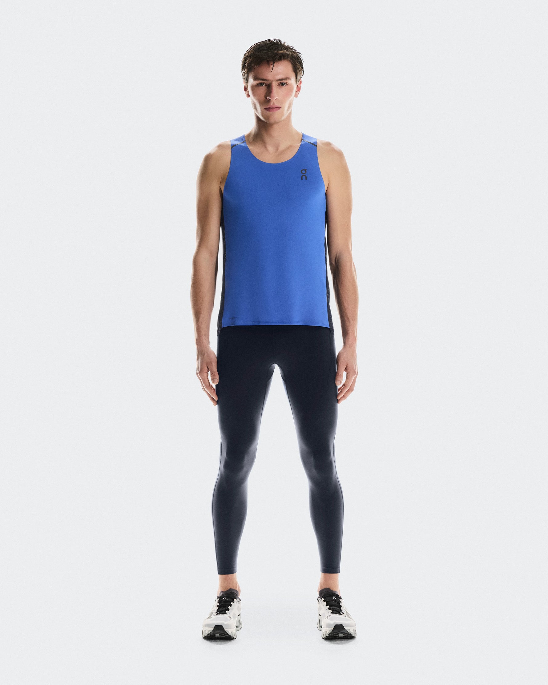 Man wearing blue On Performance Tank with navy leggings in studio photo