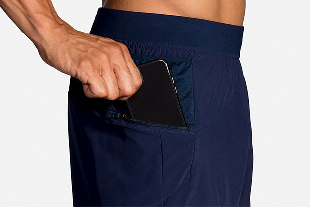 Brooks Sherpa 5-inch men's navy shorts with zippered pocket holding a smartphone