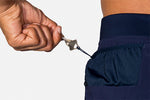 Hand pulling keys from secure zip pocket of Brooks Sherpa navy running shorts
