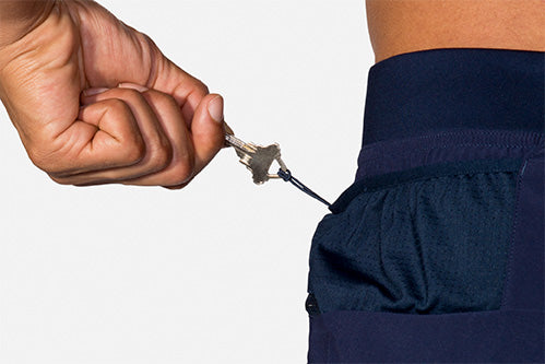 Hand pulling keys from secure zip pocket of Brooks Sherpa navy running shorts
