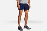 Brooks Sherpa 5-inch 2-in-1 men's running shorts in navy blue with gray sneakers
