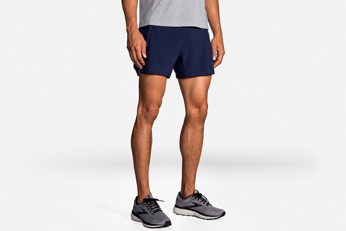 Brooks Sherpa 5-inch 2-in-1 men's running shorts in navy blue with gray sneakers