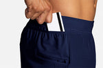 Man placing card into side pocket of Brooks Sherpa 5-inch navy running shorts