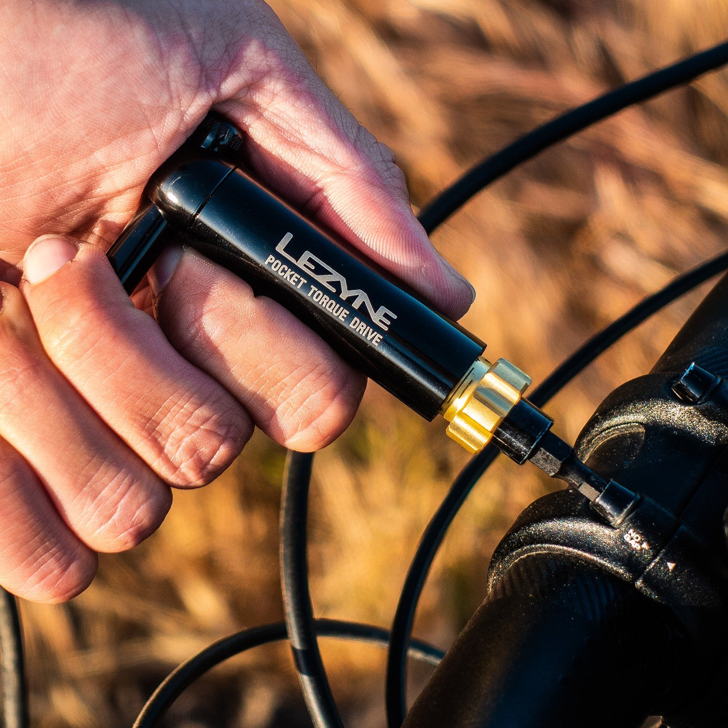 Hand holding black Lezyne Pocket Torque Drive multi-tool near bicycle wheel