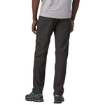 Man wearing dark green Patagonia Quandary pants with hiking shoes on white background