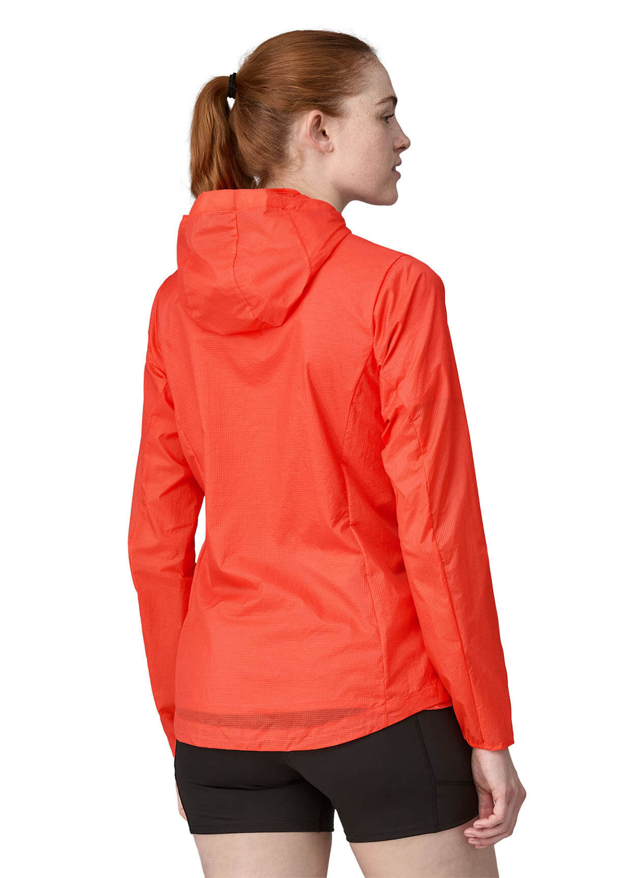 Woman wearing bright coral Patagonia Houdini jacket, back view showing hood and fitted design