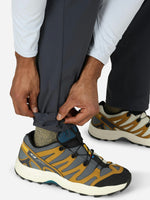 Person adjusting gray convertible pants leg while wearing outdoor hiking shoes