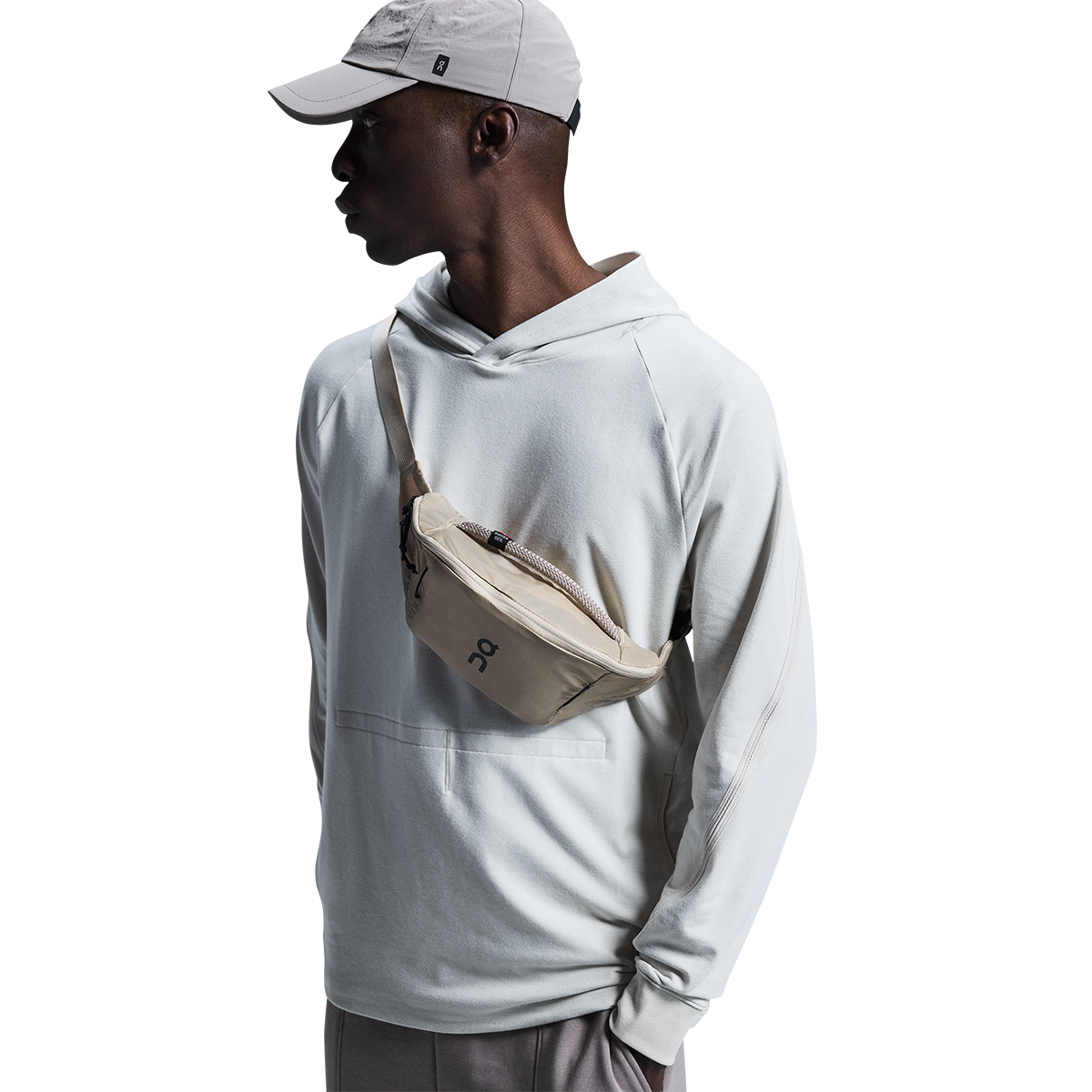 Model wearing beige On waist pack across chest with gray hoodie and cap