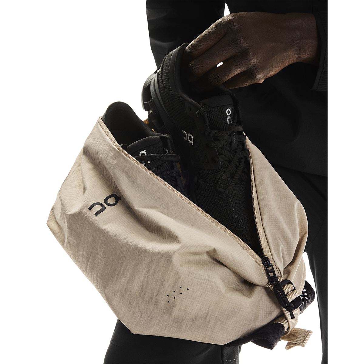 On Sling Pack 9L in Biscuit being loaded with black On running shoes