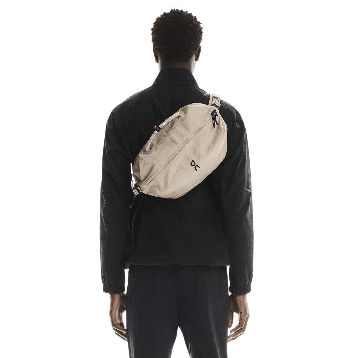 On Sling Pack 9L in Biscuit worn crossbody on model's back, studio shot