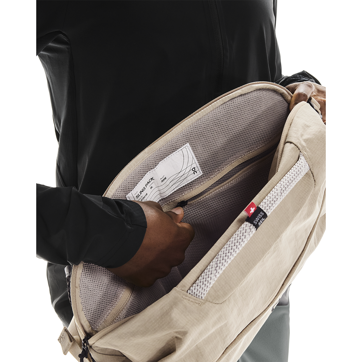 On Sling Pack 9L in Biscuit opened to reveal interior mesh compartments and Swiss Seil label