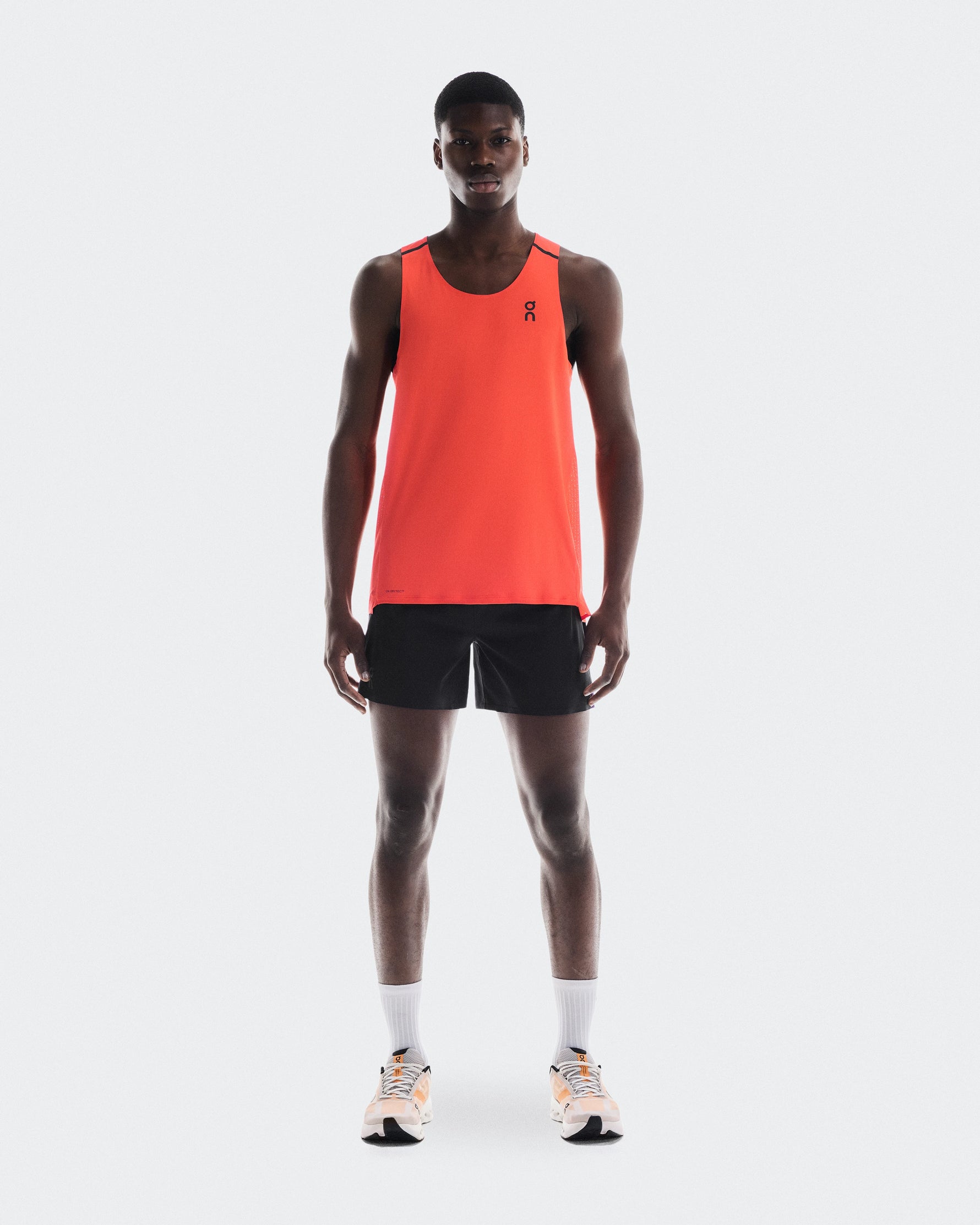 Man wearing bright orange On Performance Tank with black shorts and running shoes