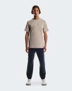 Man wearing beige On Core-T shirt with navy joggers in studio setting