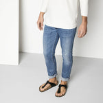 Man wearing black Birkenstock Gizeh sandals with jeans in studio setting