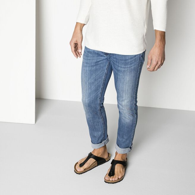 Man wearing black Birkenstock Gizeh sandals with jeans in studio setting