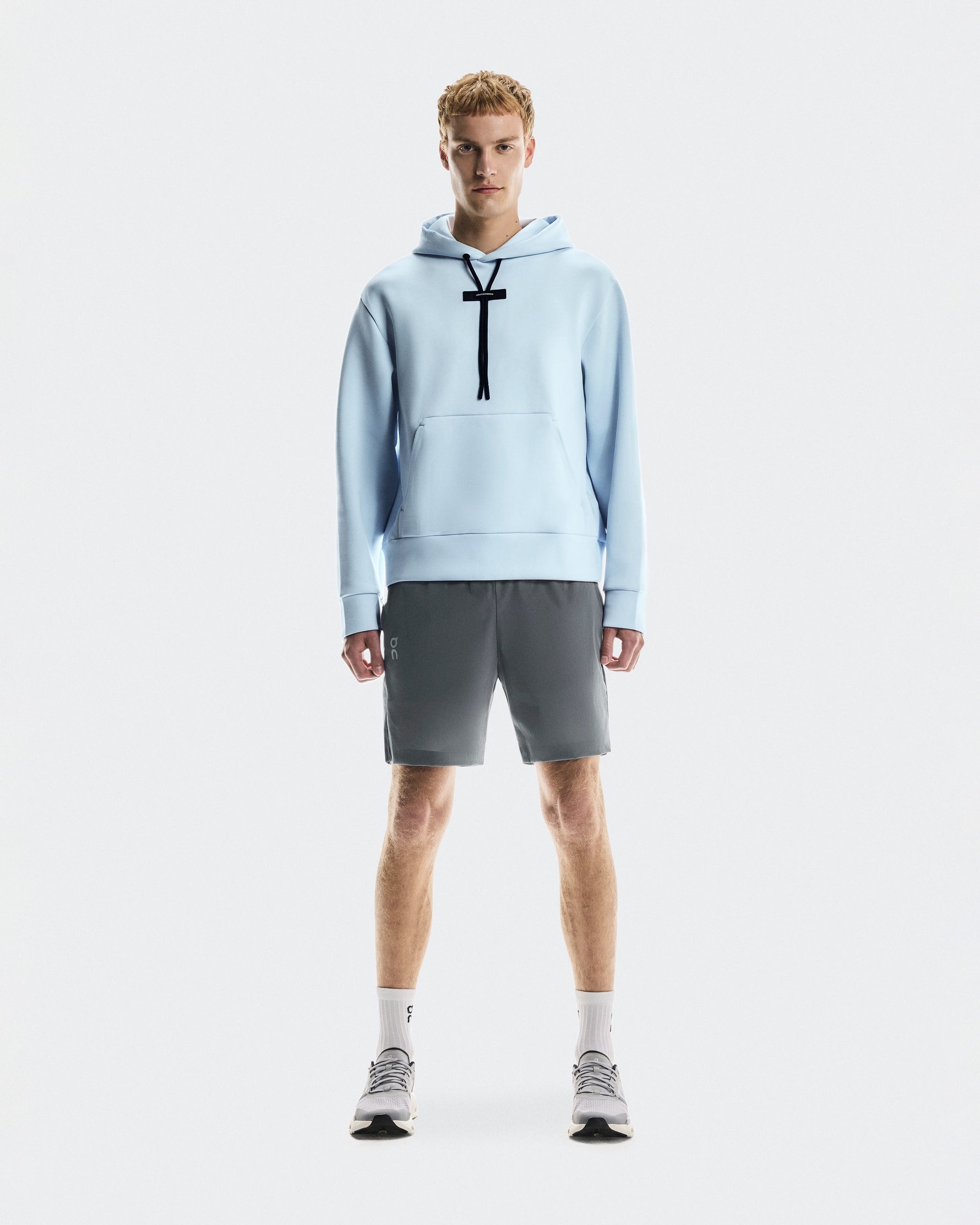 Male model wearing light blue On Focus Tech Hoodie with gray shorts and sneakers