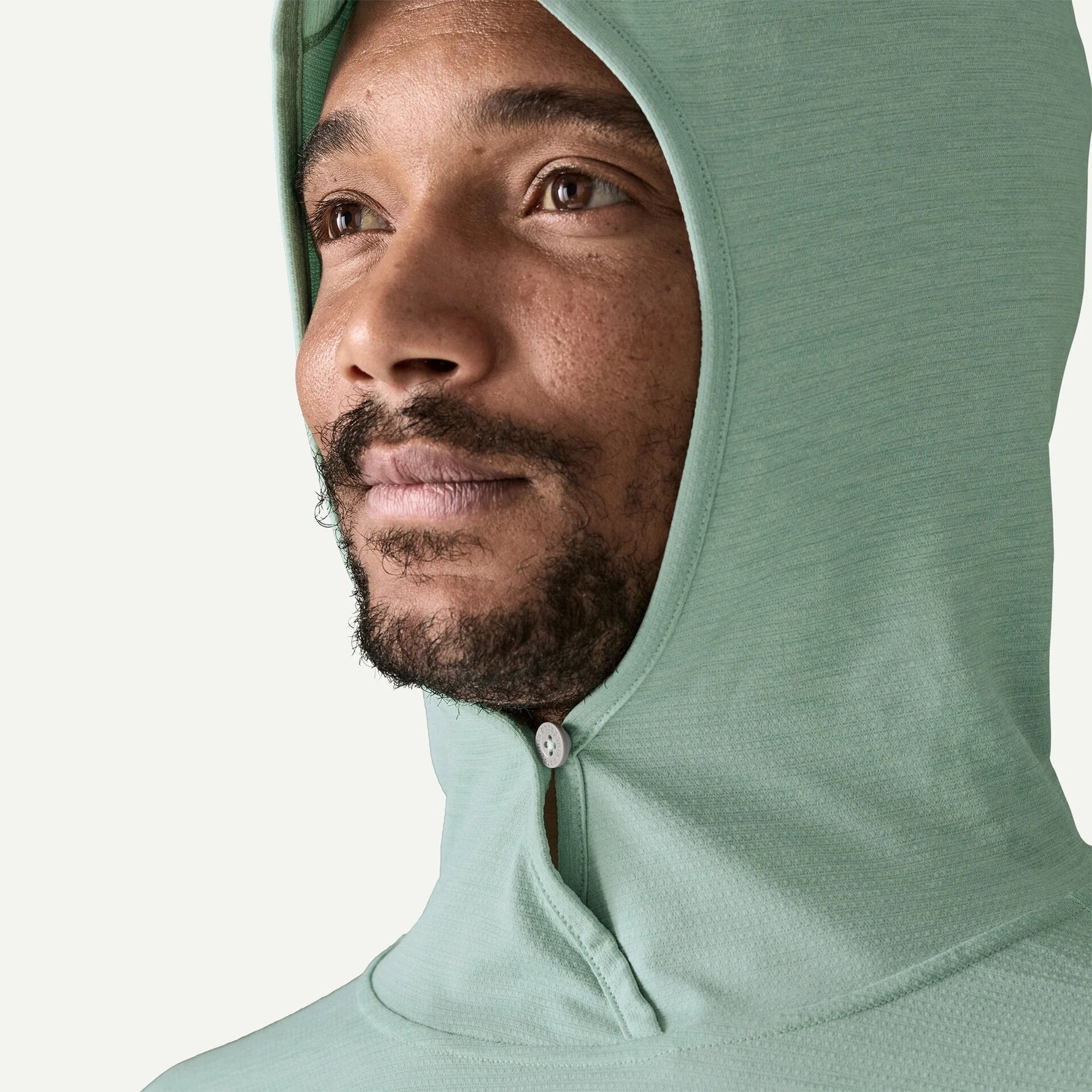 Man wearing sage green Patagonia sun hoody with hood up against white background