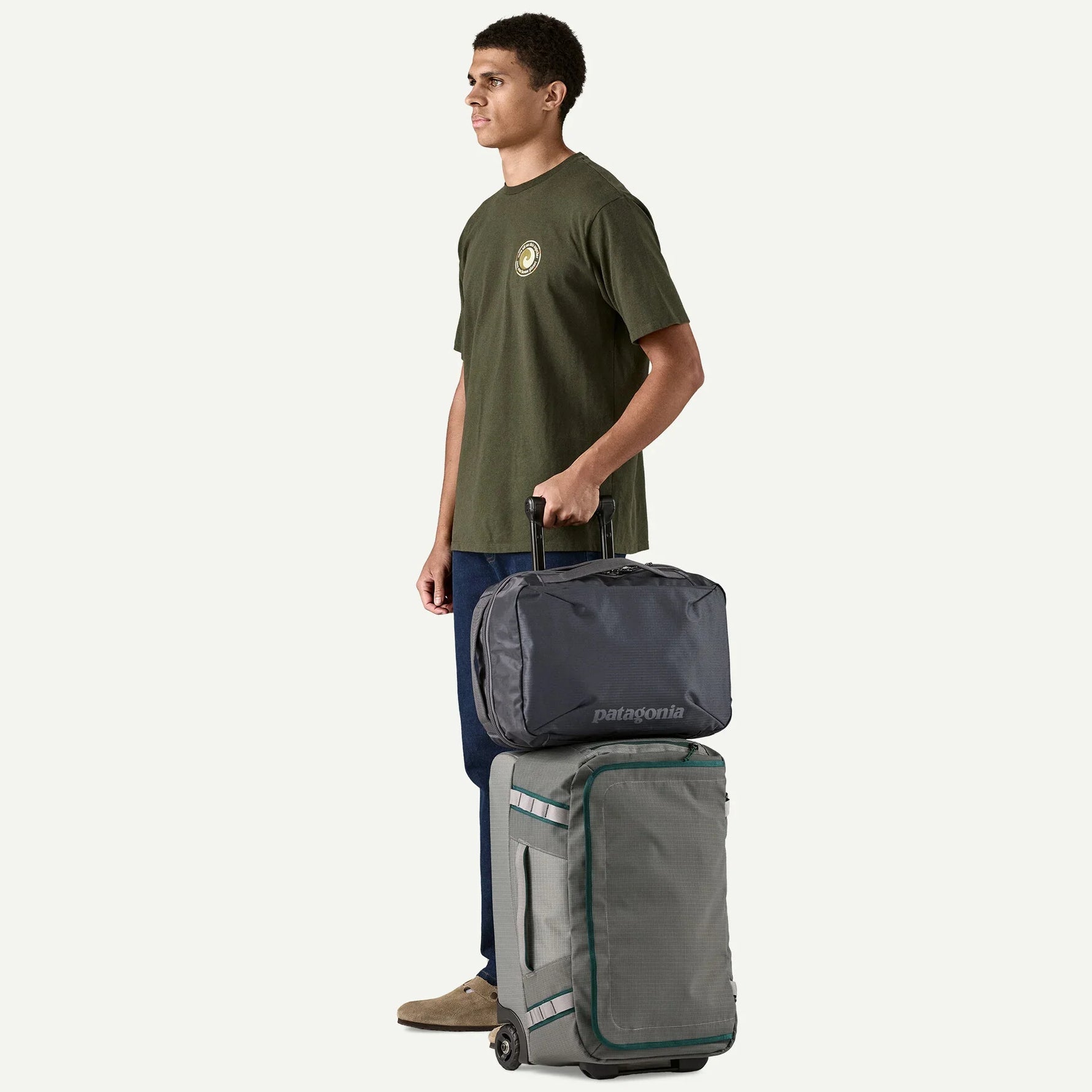 Man holding Patagonia Black Hole MLC rolling luggage in noble grey color