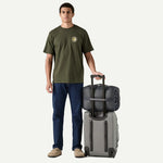 Man holding Patagonia Black Hole MLC travel bag in Noble Grey with wheeled luggage