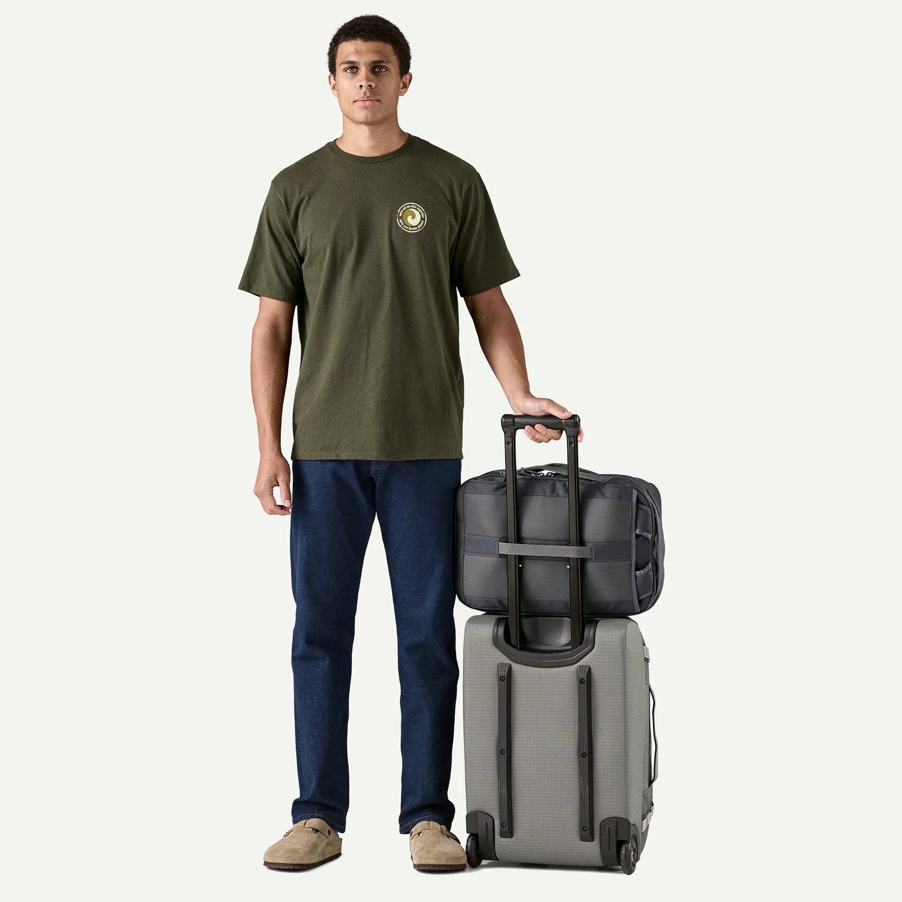 Man holding Patagonia Black Hole MLC travel bag in Noble Grey with wheeled luggage