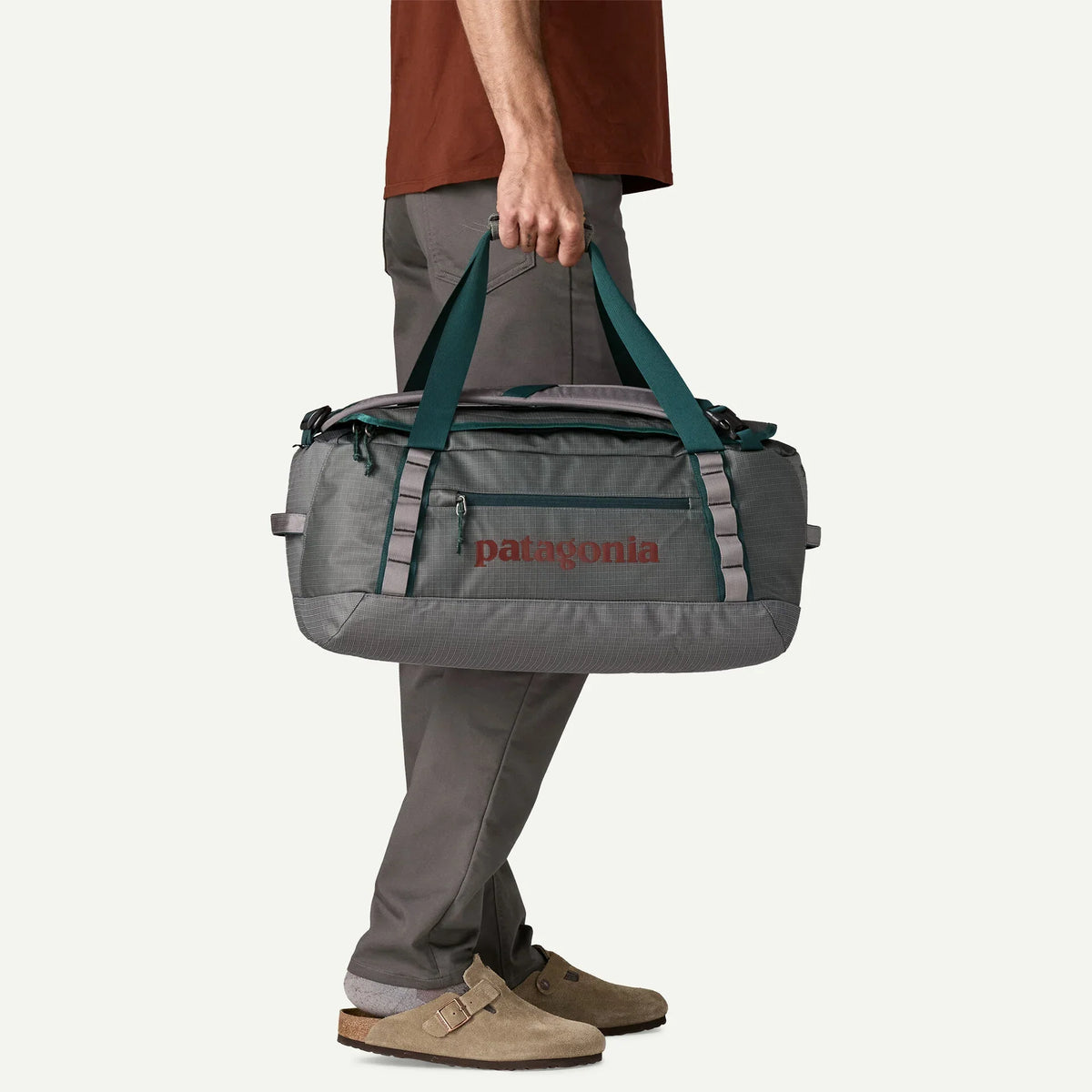 Man holding Patagonia Black Hole 40L duffel bag by teal handles, Noble Grey colorway, side view