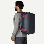 Man wearing Patagonia Black Hole Duffel 40L backpack in smolder blue with red straps