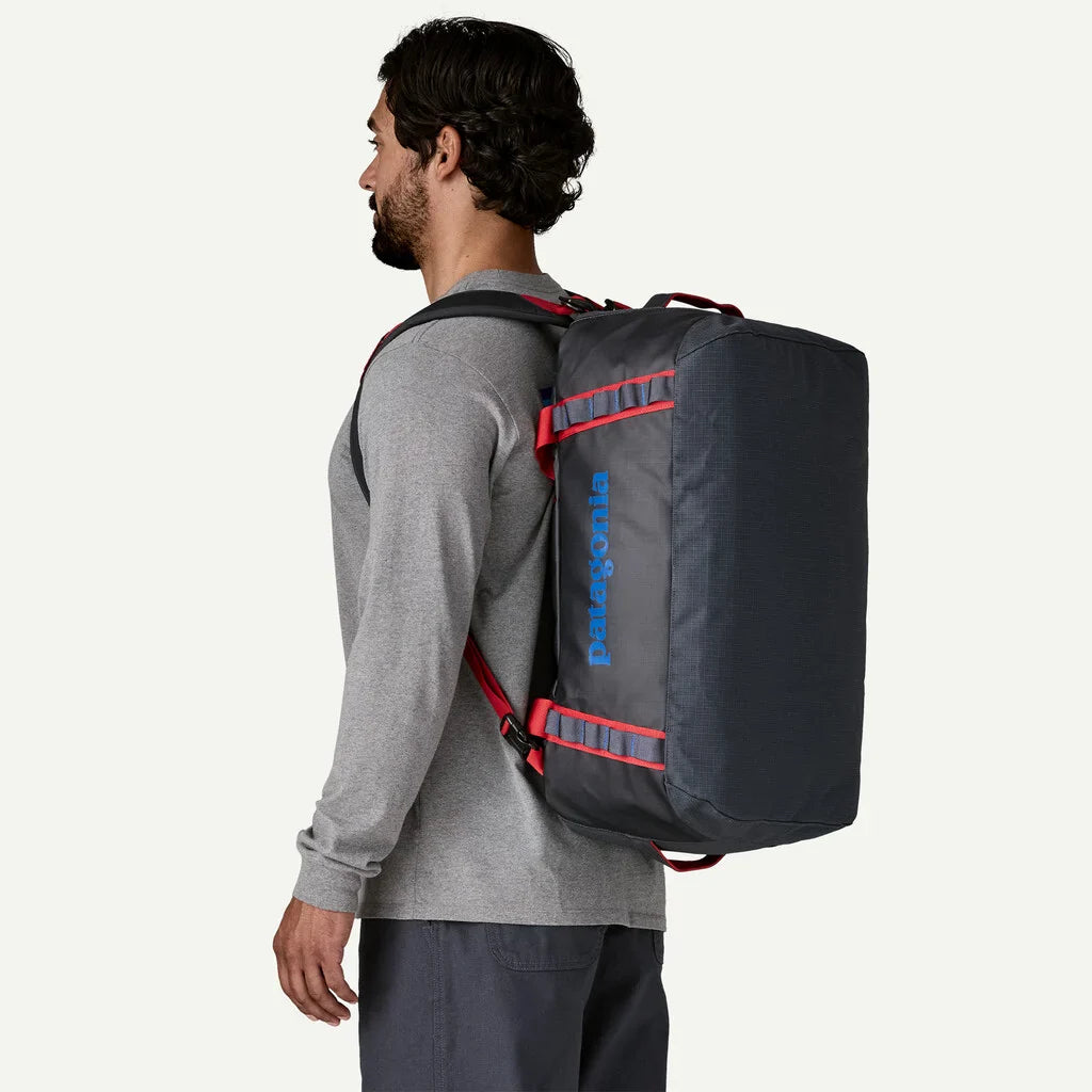 Man wearing Patagonia Black Hole Duffel 40L backpack in smolder blue with red straps